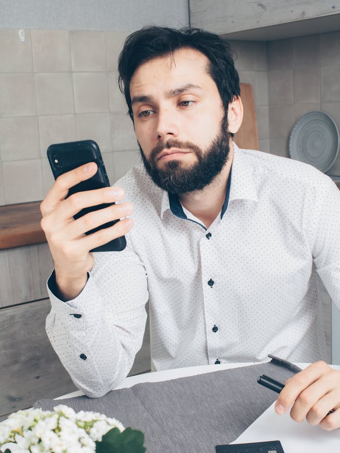 pexels-photo-7534742 A man looks frustrated while checking his smartphone, possibly experiencing a banking issue or scam.